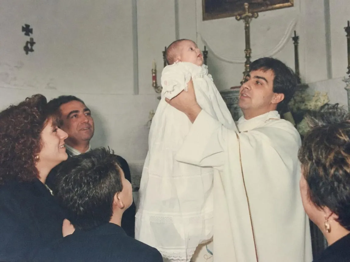 A young priest holding a baby up at a baptism in a small parish church