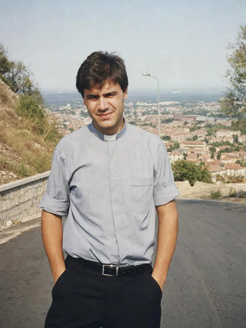 A young priest standing on a hill road above a town, 1996