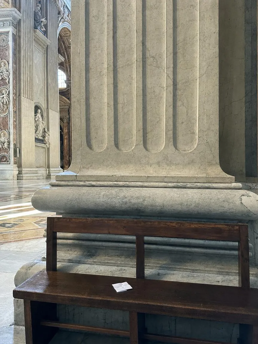 An empty wooden bench against a marble pier inside St. Peter's Basilica